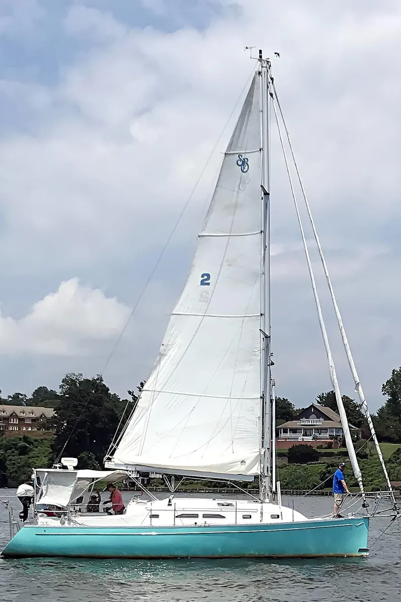 Slide: The Image of 2005 Shannon Shoalsailer sailboat on water with white sails and turquoise hull. - 22
