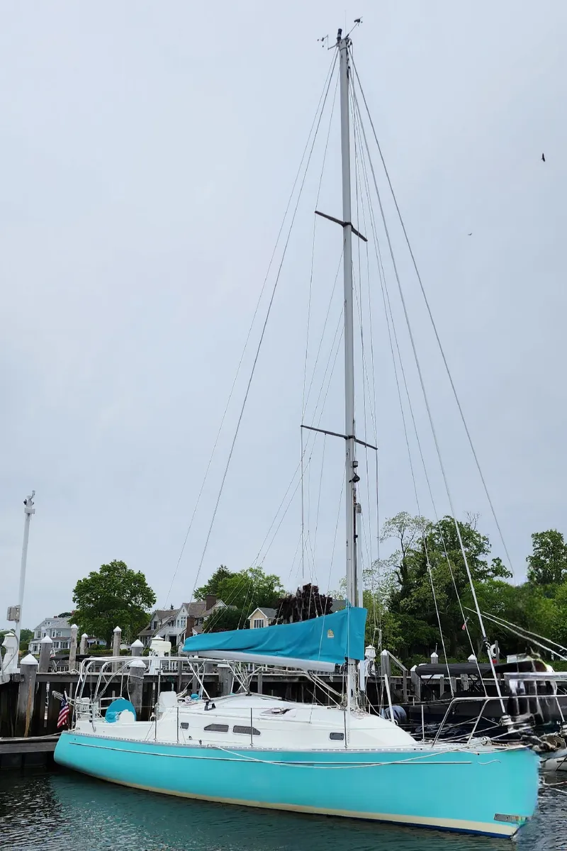 Slide: The Image of 2005 Shannon Shoalsailer sailboat docked, featuring a turquoise hull and tall mast. - 5