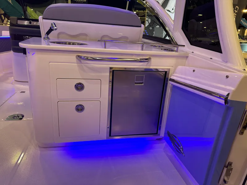 Slide: The Image of 2025 Chaparral 310 OSX boat interior with kitchenette, featuring drawers, fridge, and blue LED lighting. - 10