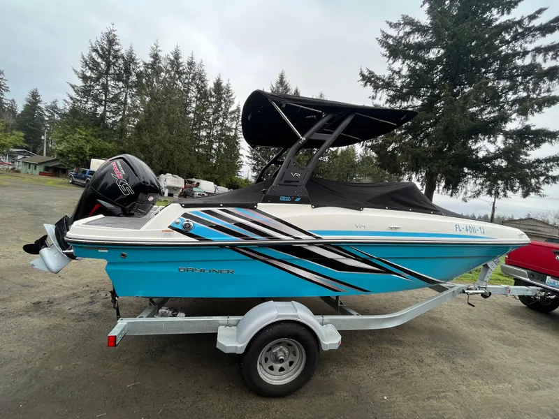 Slide: The Image of 2023 Bayliner VR4 Bowrider OB on trailer, parked outdoors with trees in background. - 19