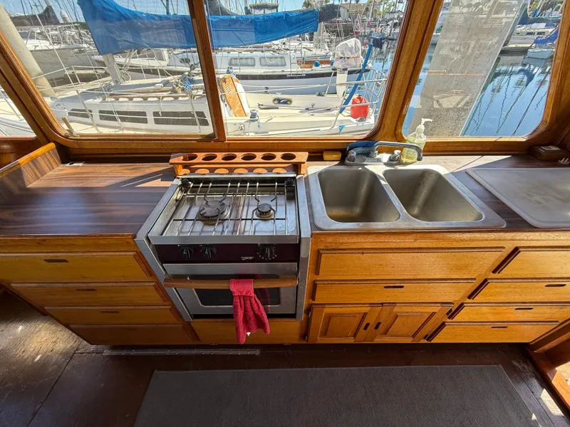 Slide: The Image of 1983 Californian 34 yacht kitchen with stove, sink, and wooden cabinetry overlooking marina. - 28