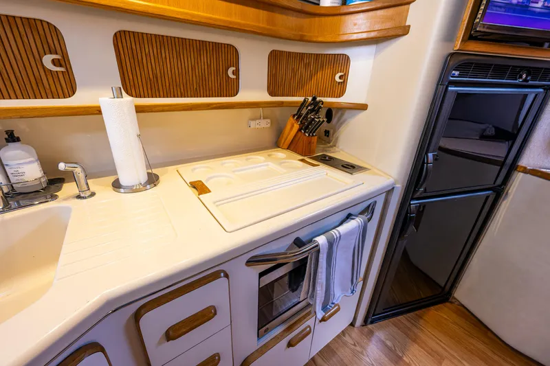 Slide: The Image of 1991 Sea Ray 420 Sundancer kitchen with sink, stove, and fridge in a compact layout. - 33