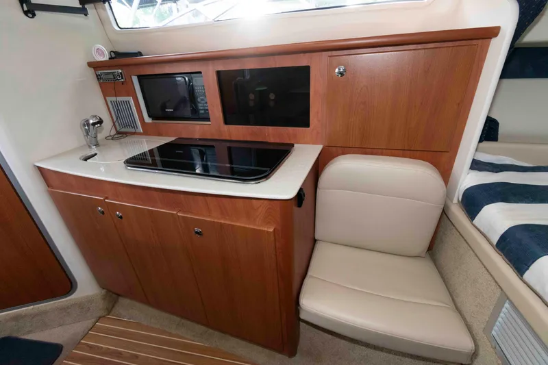 Slide: The Image of 2008 Bayliner 285 interior with kitchenette, featuring wood cabinets, stove, and seating. - 6