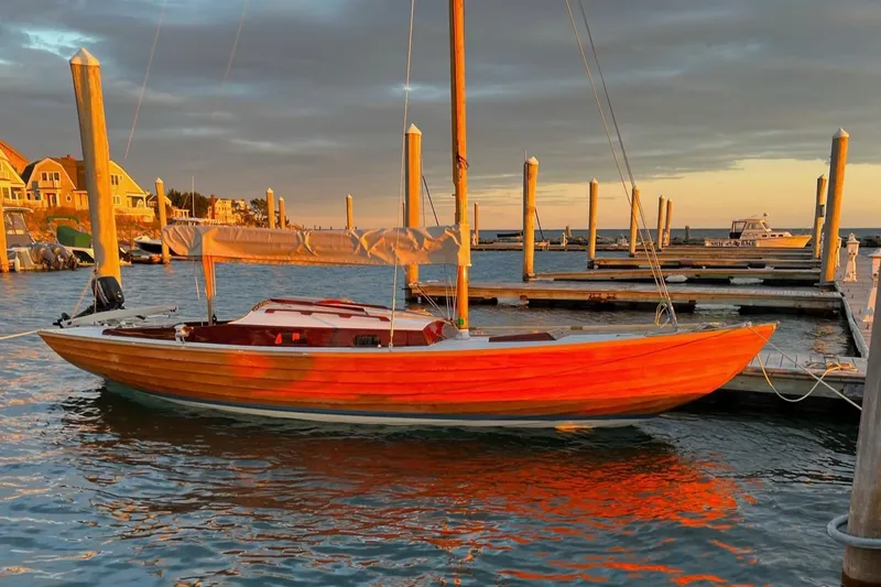 The Image of 1979 Nordic Folkboat docked at sunset, reflecting warm orange hues on the water. - 0