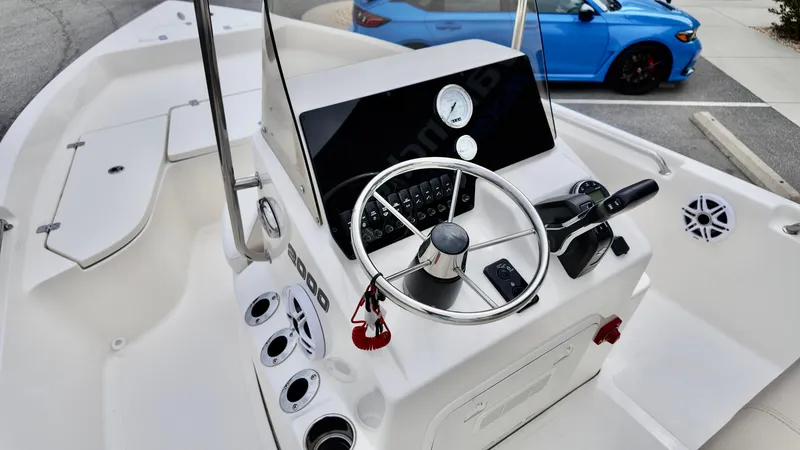 Slide: The Image of 2025 Bulls Bay 2000 boat console with steering wheel and controls, parked near a blue car. - 11