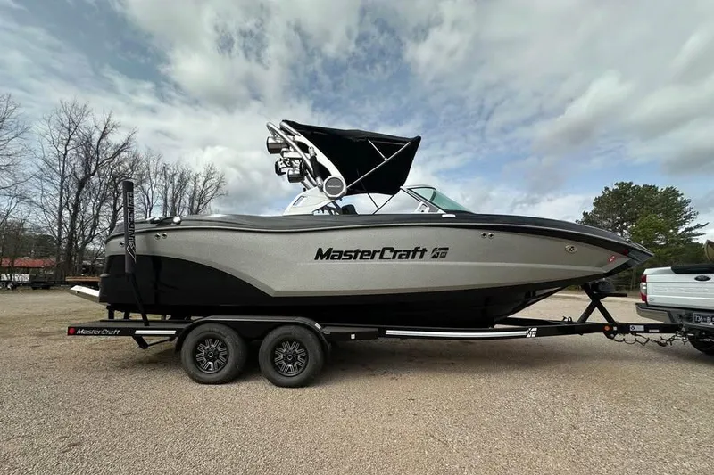 The Image of 2021 MasterCraft XT22 boat on trailer, parked outdoors under cloudy sky. - 0