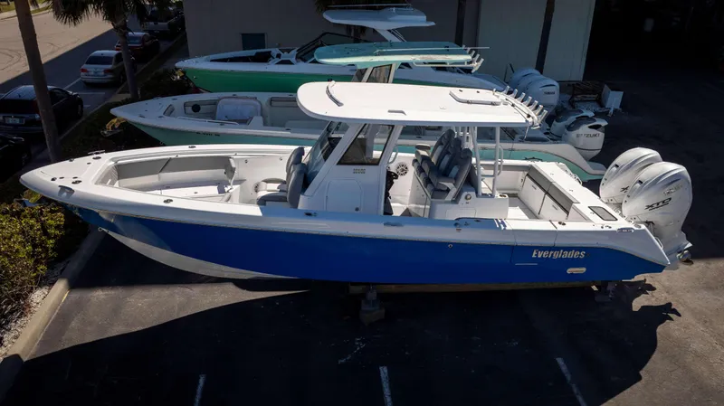 Slide: The Image of 2025 Everglades 335 CC boat with blue hull, parked outdoors, featuring twin engines. - 1