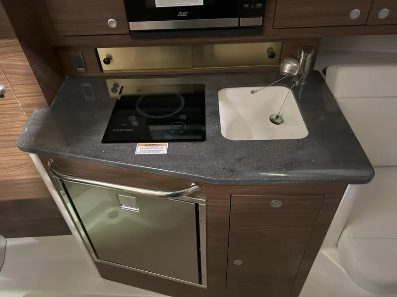 Slide: The Image of 2025 Boston Whaler 325 Conquest galley with stove, sink, and compact refrigerator. - 10