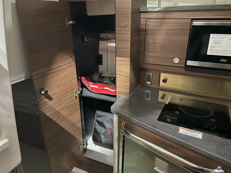 Slide: The Image of Interior of 2025 Boston Whaler 325 Conquest, featuring a compact kitchen with storage and appliances. - 14
