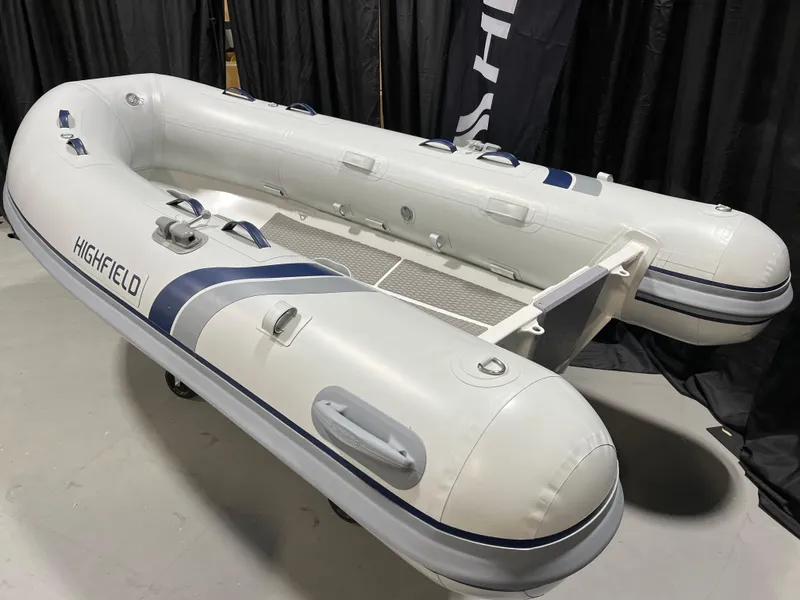 Slide: The Image of 2025 Highfield Ultralite 310 inflatable boat, white with blue accents, displayed indoors. - 2