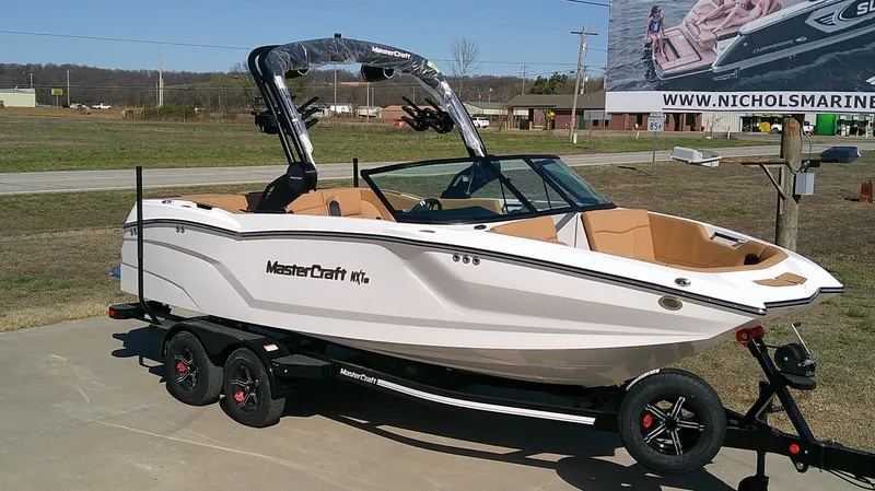 Slide: The Image of 2025 MasterCraft NXT22 boat on trailer, displayed outdoors at a dealership. - 2