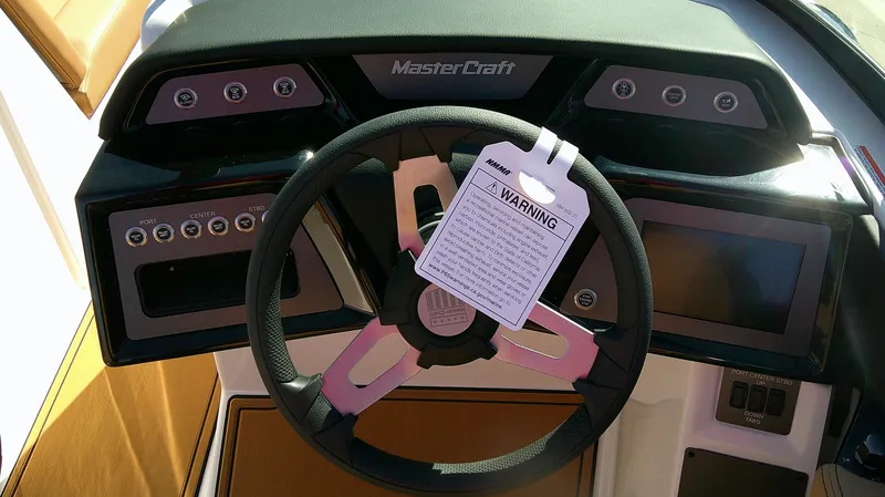 Slide: The Image of 2025 MasterCraft NXT22 boat dashboard with steering wheel and warning tag. - 8