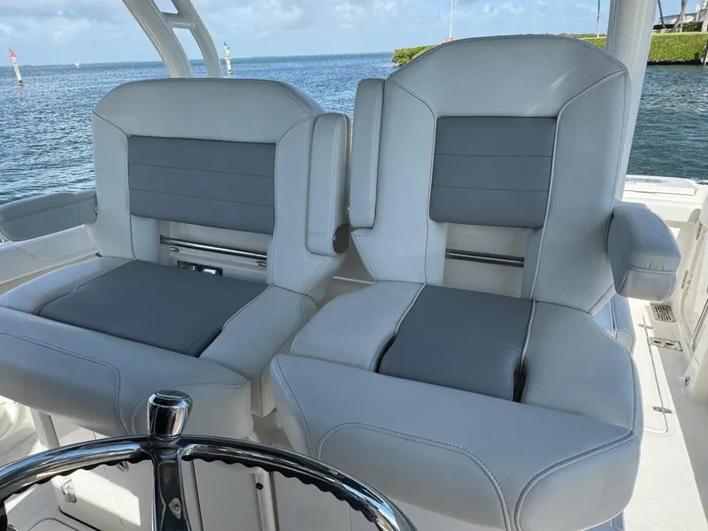 Slide: The Image of 2022 Pursuit S 328 Sport boat seats with gray upholstery, steering wheel visible, ocean backdrop. - 8