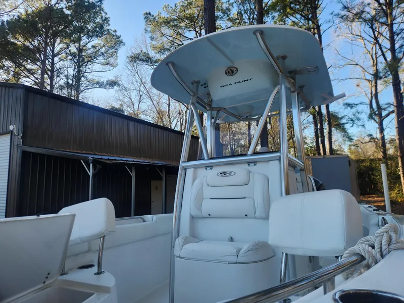 Slide: The Image of 2016 Sea Hunt Ultra 225 boat with T-top, docked near trees and a building. - 8