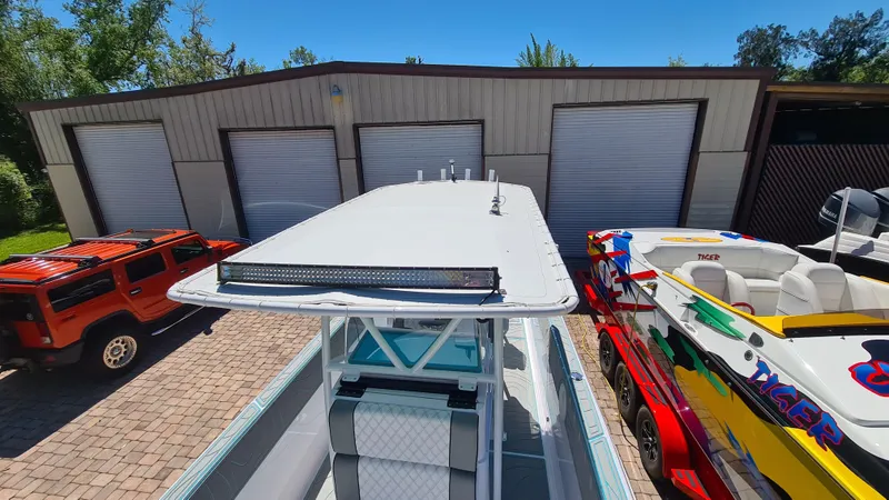 Slide: The Image of 2025 Custom Core 38 Center Console boat parked between vehicles near a garage. - 24