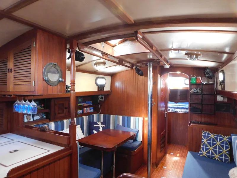 Slide: The Image of 1984 Tayana 37 yacht interior with wooden finish, dining area, and cozy seating. - 6