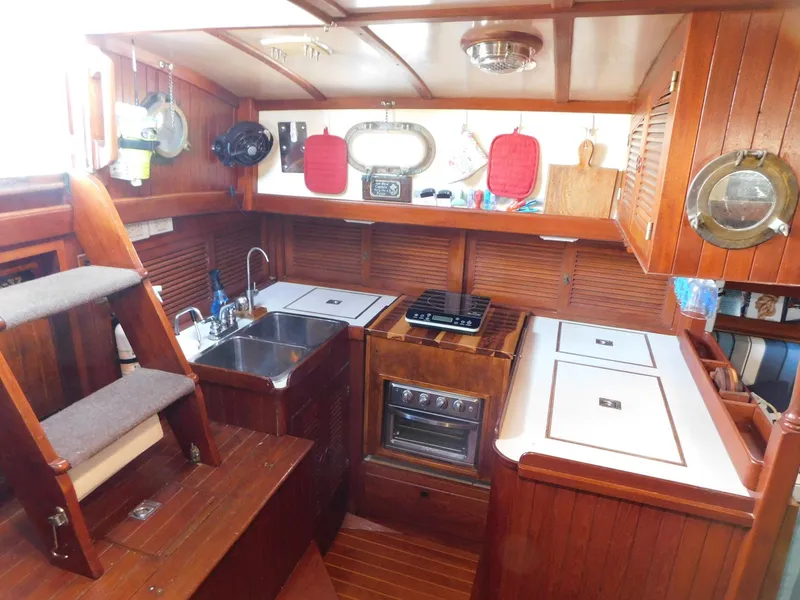 Slide: The Image of 1984 Tayana 37 yacht interior kitchen with wood finish, stainless steel sink, and compact stove. - 9