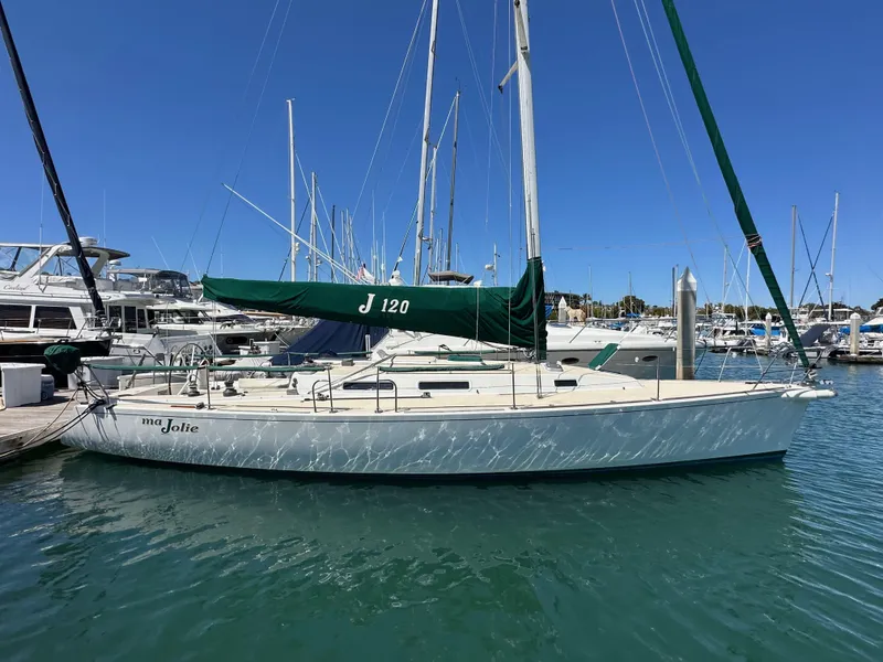 Slide: The Image of 1996 J Boats J/120 sailboat docked in marina, green sail cover, clear blue sky. - 1