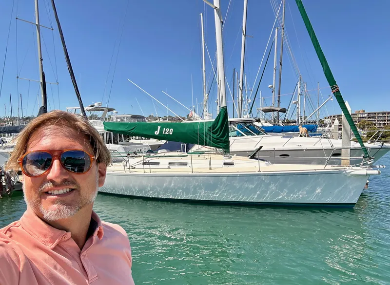 Slide: The Image of Man smiling in front of a 1996 J Boats J/120 sailboat at a marina. - 2