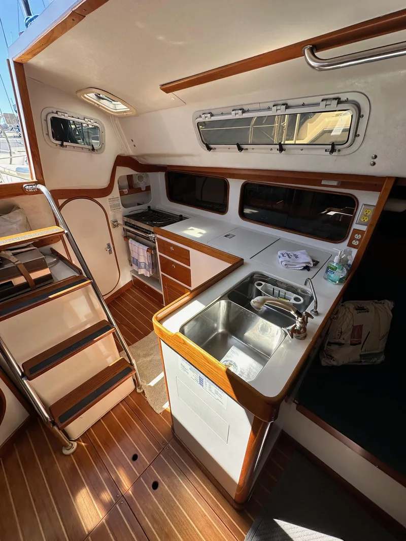 Slide: The Image of Interior of a 1996 J Boats J/120 sailboat, featuring a compact kitchen and wooden flooring. - 38