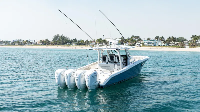 Slide: The Image of 2021 Pursuit 428 boat with four engines on calm water near a beach. - 1