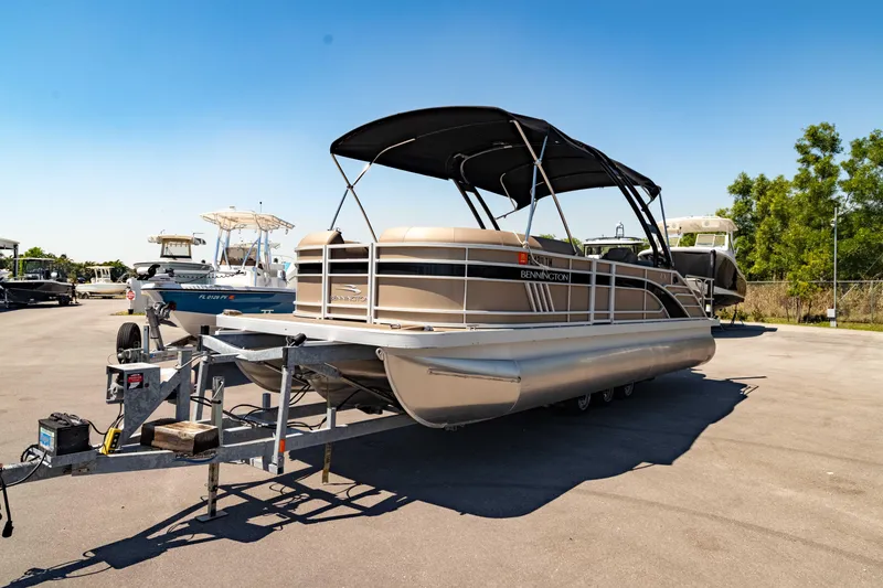 Slide: The Image of 2022 Bennington LX 24 Swingback pontoon boat on trailer, parked outdoors under clear sky. - 11