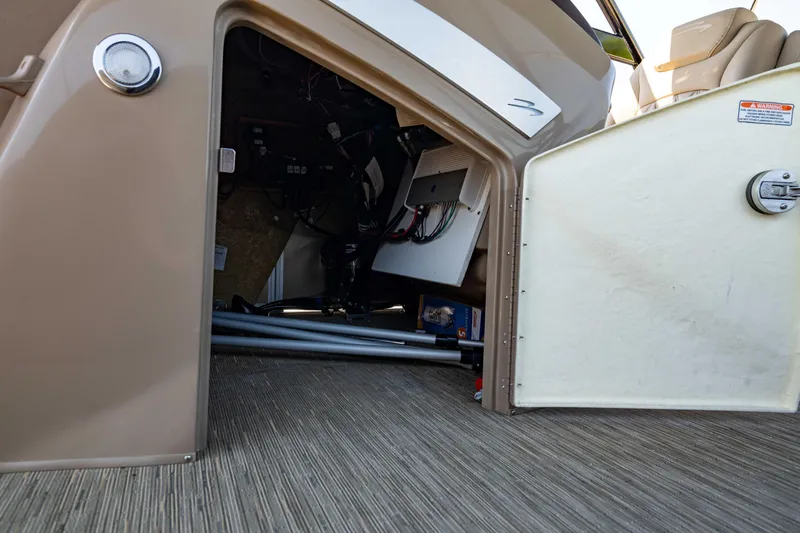 Slide: The Image of 2022 Bennington LX 24 Swingback storage compartment with open door, revealing interior components. - 28