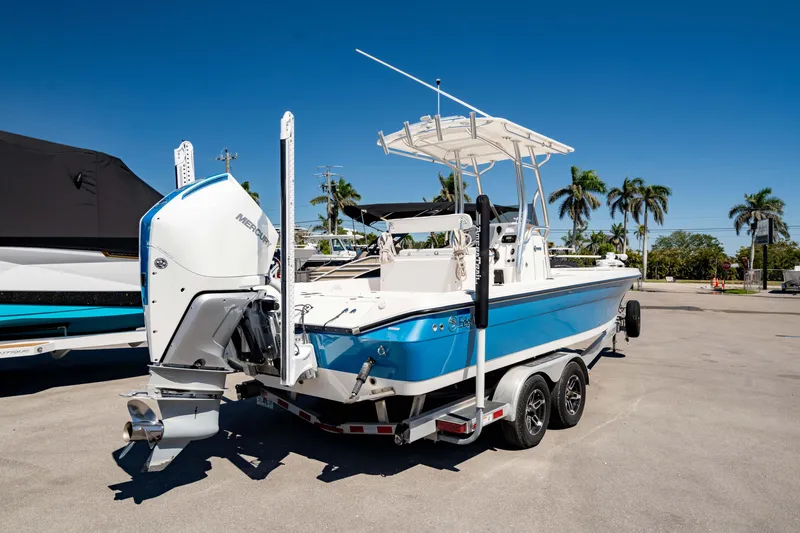 Slide: The Image of 2015 Edgewater 240 Inshore boat on trailer, blue hull, palm trees in background. - 45