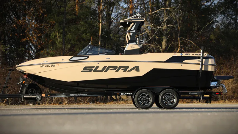 Slide: The Image of 2023 Supra SL boat on trailer, parked outdoors with forest background. - 13