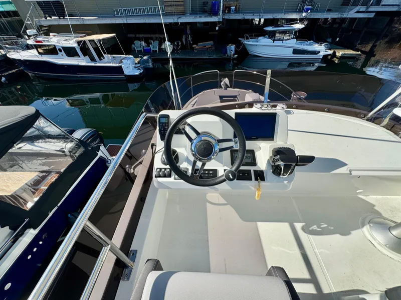 Slide: The Image of 2023 Jeanneau NC 1095 Flybridge helm with steering wheel and controls, docked at marina. - 18