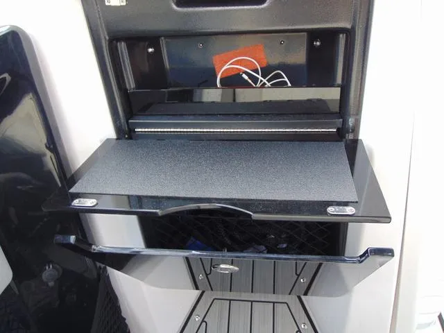 Slide: The Image of 2023 Yamaha Boats 252SD storage compartment with fold-out shelf and netted storage area. - 18