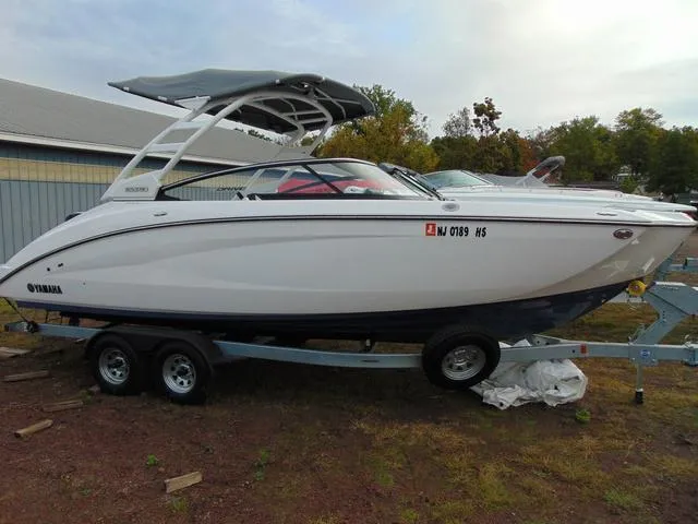 Slide: The Image of 2023 Yamaha Boats 252SD on trailer, sleek design, white exterior, parked outdoors. - 2
