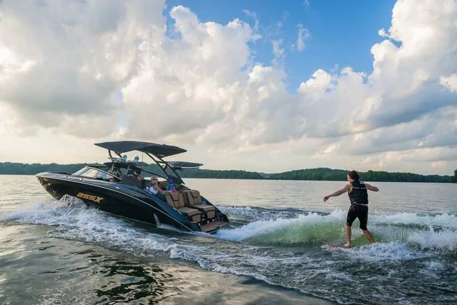 Slide: The Image of 2025 Yamaha Boats 255XD on lake, person wakesurfing behind, under cloudy sky. - 12