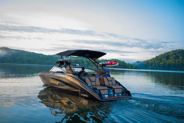 Slide: The Image of 2025 Yamaha Boats 255XD cruising on a serene lake with lush green hills. - 13