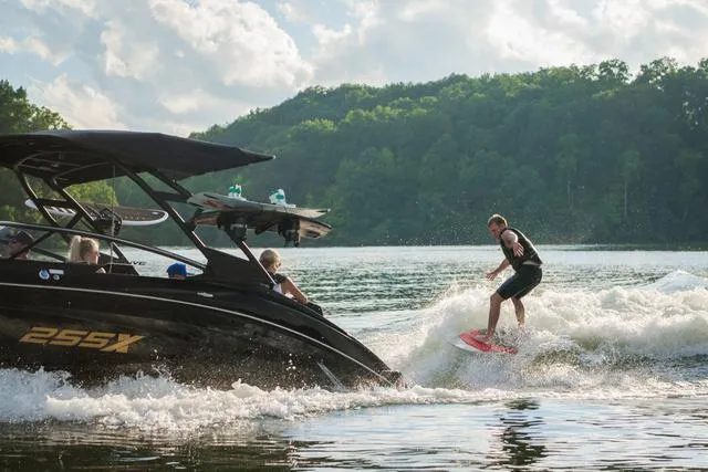 Slide: The Image of 2025 Yamaha Boats 255XD creating waves for a wakeboarder on a scenic lake. - 14