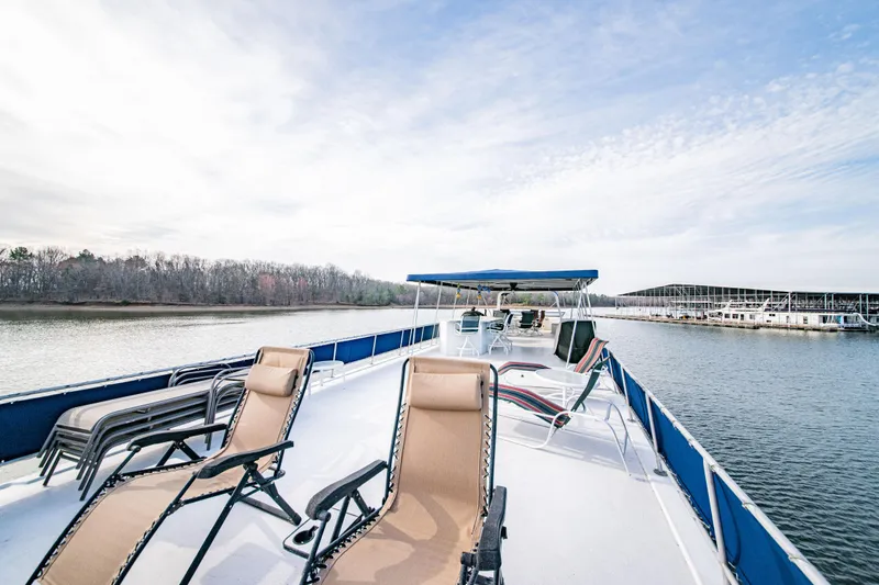 Slide: The Image of 1997 Stardust Cruisers 72x16 houseboat with deck chairs on a serene lake. - 17