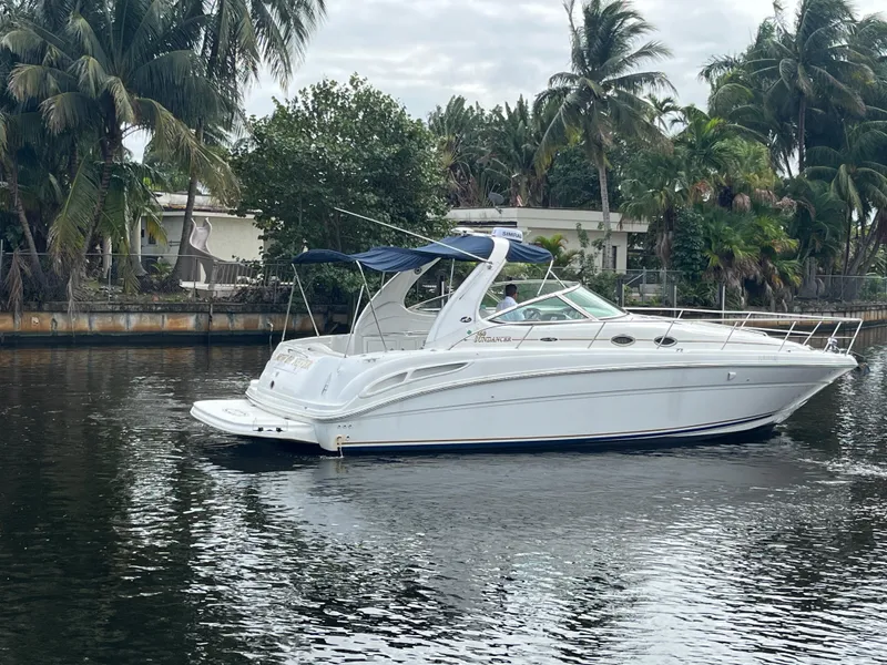 Slide: The Image of 2003 Sea Ray 360 Sundancer yacht on a calm waterway, surrounded by lush palm trees. - 2