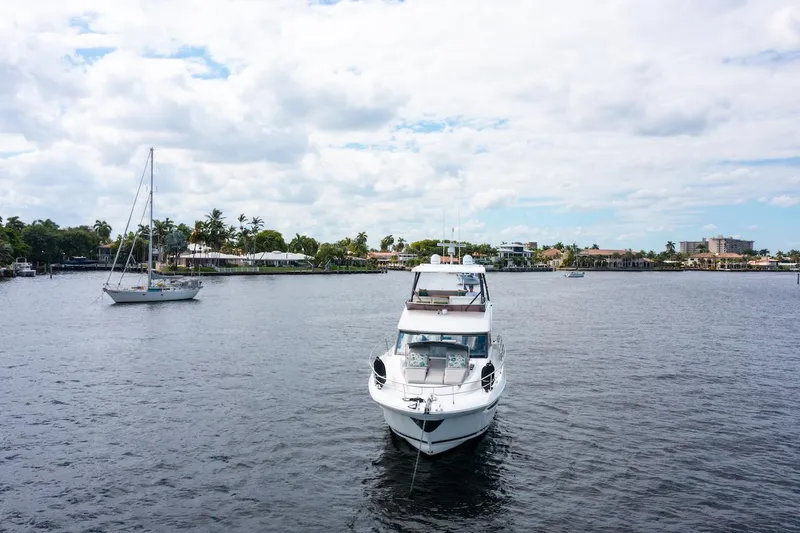 Slide: The Image of Prestige 520 Fly yacht on calm water, 2020 model, with sailboats and cloudy sky. - 3