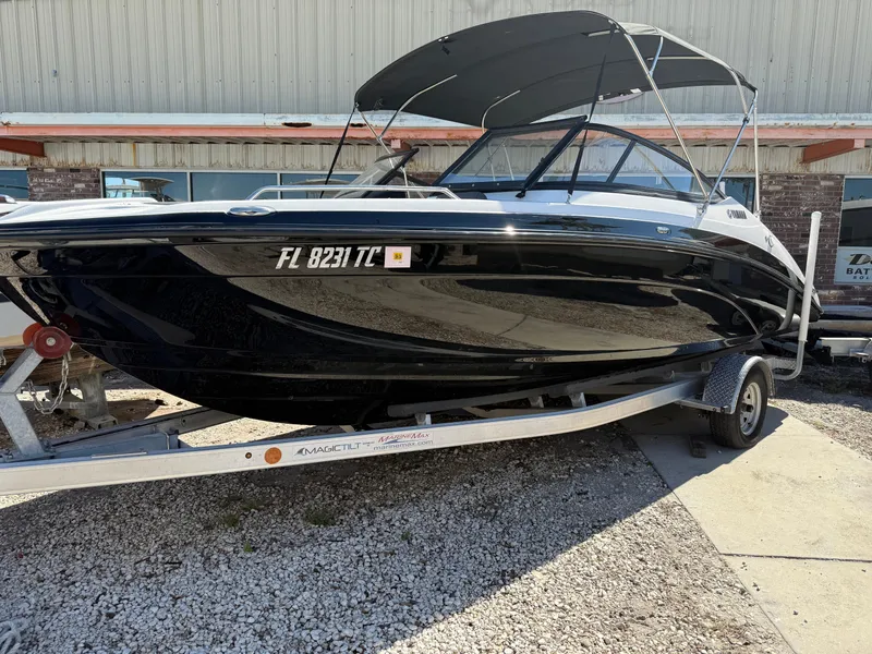 The Image of 2022 Yamaha SX210 boat on trailer, black hull, parked outdoors. - 1