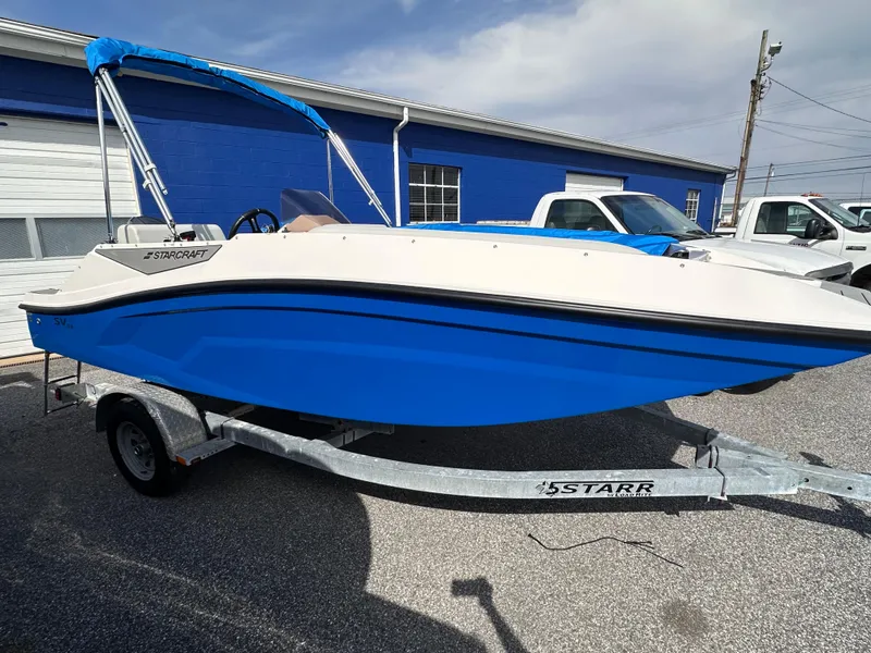The Image of 2025 Starcraft SV 16 OB boat with blue hull on a trailer, parked outdoors. - 0