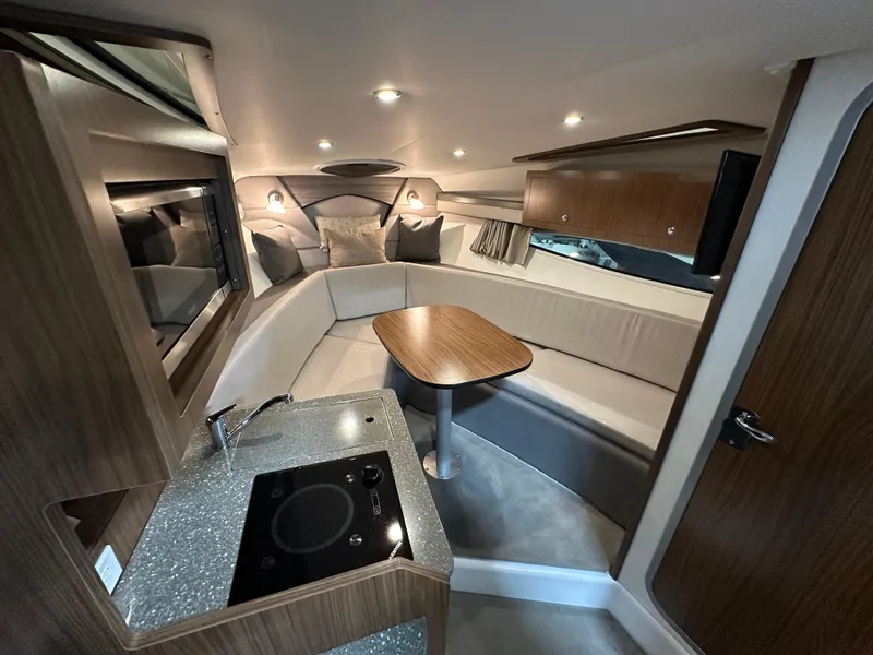 Slide: The Image of 2021 Four Winns Vista 275 cabin interior with seating, table, and kitchenette. - 16