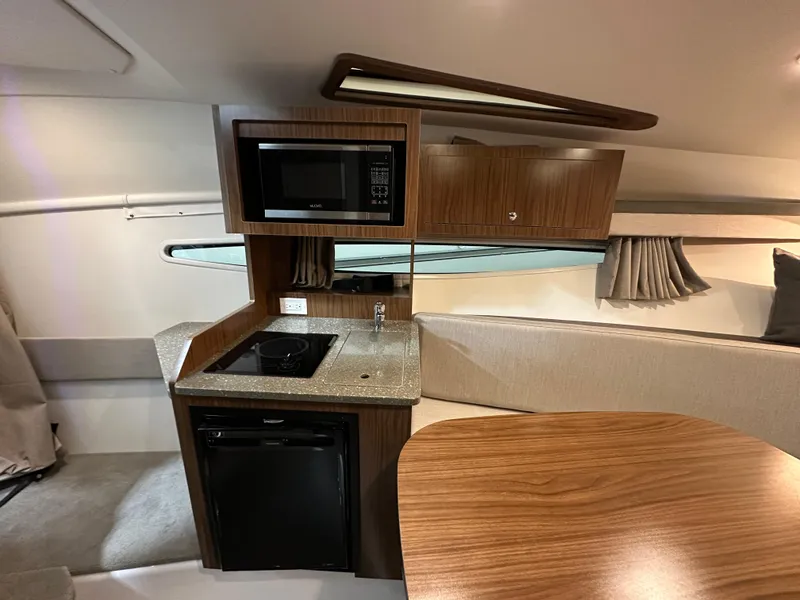 Slide: The Image of 2021 Four Winns Vista 275 interior with kitchenette, featuring microwave, stove, and compact fridge. - 17