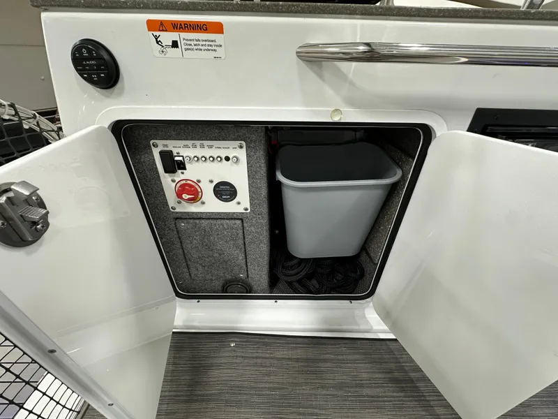 Slide: The Image of Open cabinet on 2021 Four Winns Vista 275 boat showing control panel and trash bin. - 8