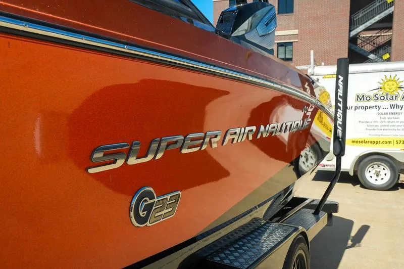 Slide: The Image of 2015 Nautique Super Air G23 boat in vibrant orange, parked outdoors. - 19