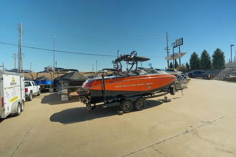 Slide: The Image of 2015 Nautique Super Air G23 boat in a parking lot, orange exterior, clear sky background. - 23
