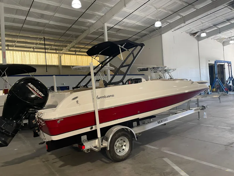 Slide: The Image of 2021 Hurricane SunDeck Sport 201 OB boat in a warehouse, featuring a red and white design. - 2