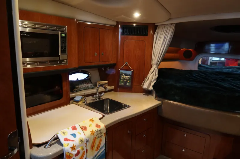 Slide: The Image of 2009 Crownline 340 CR cabin interior with kitchenette, sink, microwave, and cozy sleeping area. - 25