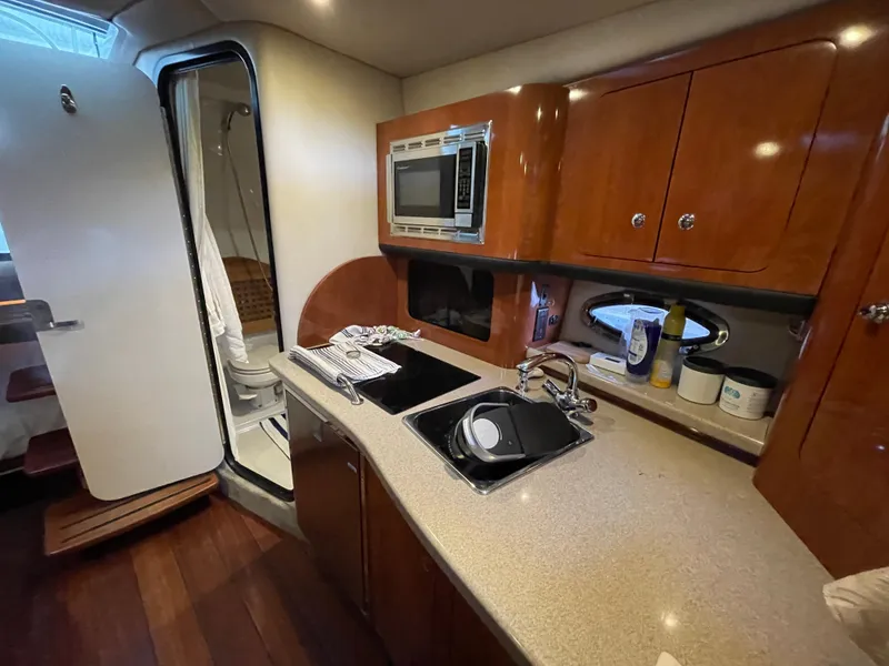 Slide: The Image of 2009 Crownline 340 CR yacht interior with kitchenette, featuring sink, microwave, and wooden cabinetry. - 49