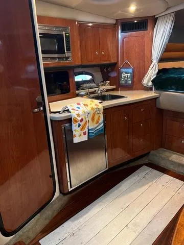 Slide: The Image of 2009 Crownline 340 CR yacht interior with kitchenette, featuring wood cabinetry and modern appliances. - 9