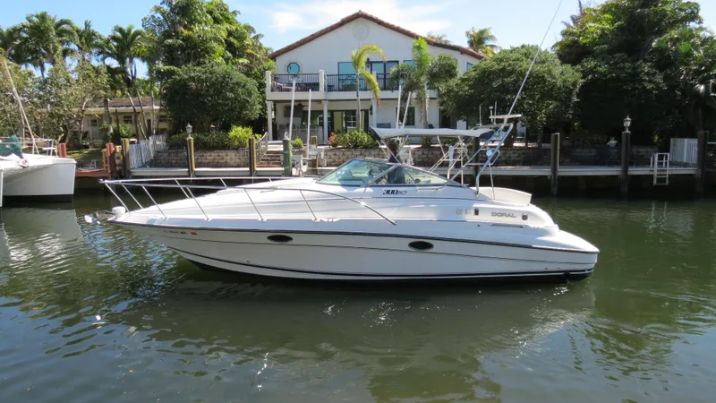 Slide: The Image of 1998 Doral 300 SC V Drive boat docked near waterfront home, surrounded by lush greenery. - 1